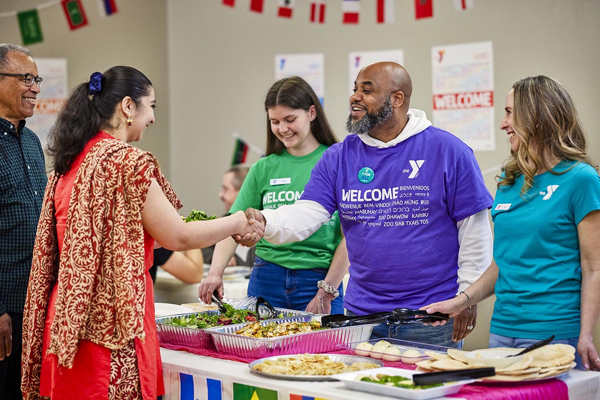 A Y staff member shakes hands with a woman while at the food station at Welcoming Week.