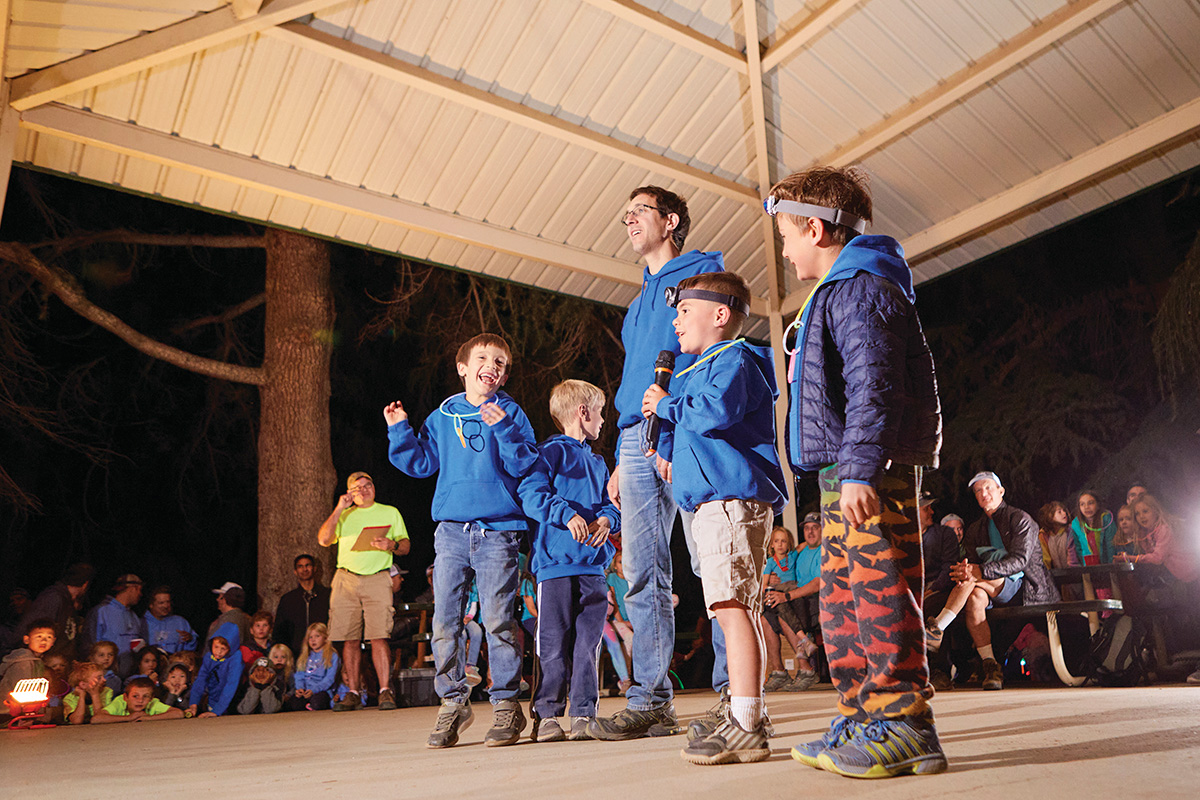 decfdb1f76a83e7c3bba7d6040e5b2dd Children playing basketball in a gym, with two players in red jerseys jumping to reach the ball and two others in purple jerseys actively participating. The YMCA logo is visible in the background, highlighting the community sports environment.